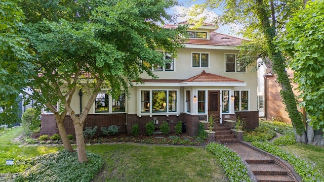 traditional style home with brick siding, a front lawn, a tile roof, and stucco siding