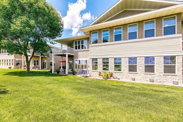 back of house with a yard, stone siding, and a balcony