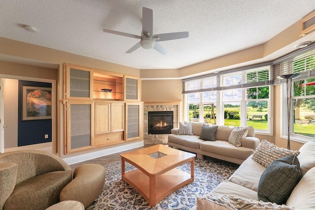 living room featuring a fireplace, a textured ceiling, a ceiling fan, and wood finished floors