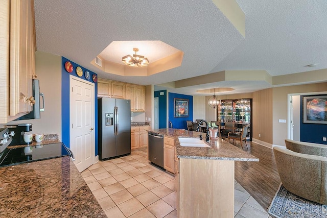 kitchen with light brown cabinetry, appliances with stainless steel finishes, an inviting chandelier, a raised ceiling, and a sink