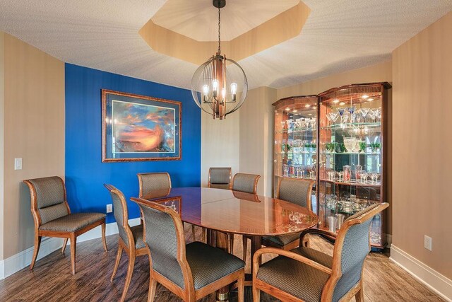 dining space featuring baseboards, an inviting chandelier, wood finished floors, a textured ceiling, and a raised ceiling