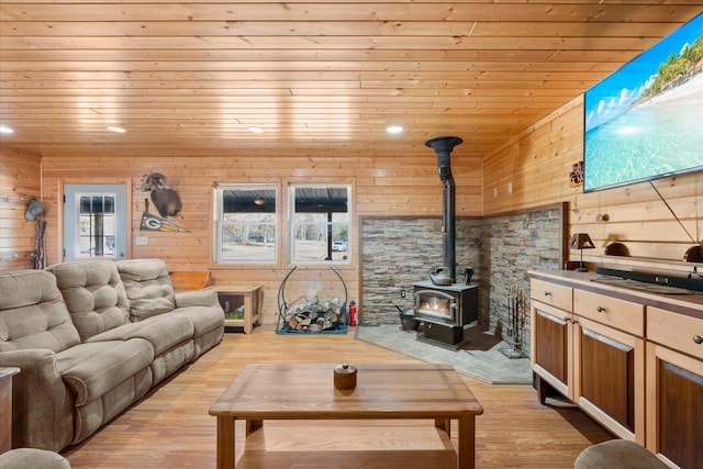 living room with wooden walls, wooden ceiling, a wood stove, and light wood-style floors