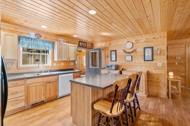 kitchen with dark countertops, a sink, a kitchen bar, and white dishwasher