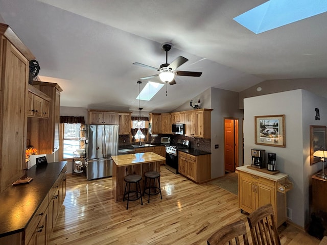 kitchen with appliances with stainless steel finishes, a breakfast bar area, a center island, a healthy amount of sunlight, and light wood-style floors