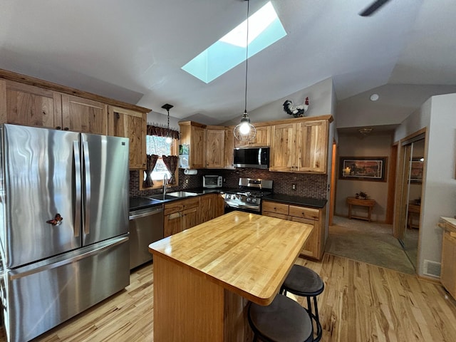 kitchen featuring tasteful backsplash, appliances with stainless steel finishes, light wood-style floors, lofted ceiling with skylight, and a sink