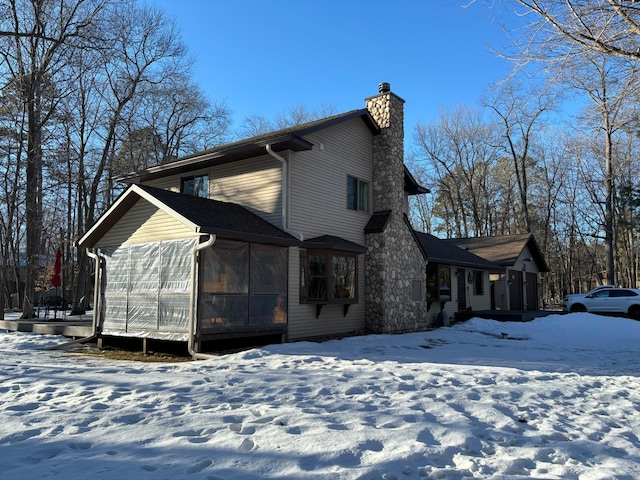 snow covered property with a sunroom, a chimney, and a wooden deck