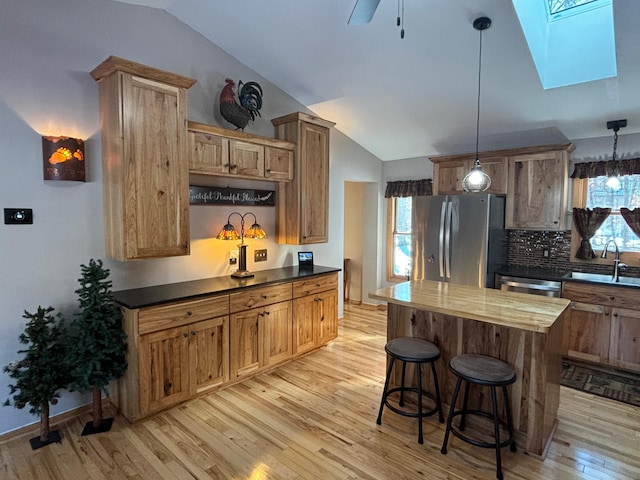 kitchen with stainless steel appliances, vaulted ceiling with skylight, light wood-type flooring, and a sink