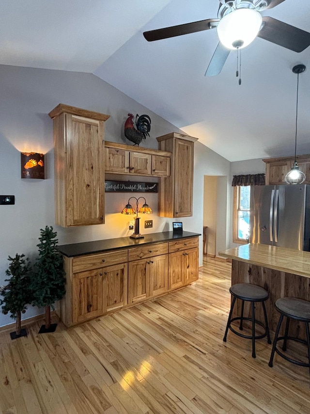 kitchen with pendant lighting, lofted ceiling, dark countertops, light wood-style flooring, and freestanding refrigerator