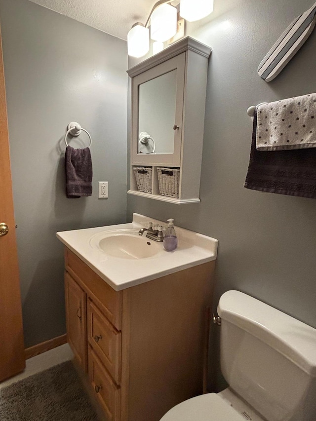 half bath with baseboards, vanity, and toilet