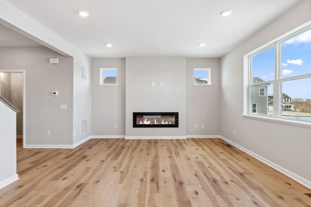 unfurnished living room with light wood finished floors, a glass covered fireplace, visible vents, and baseboards