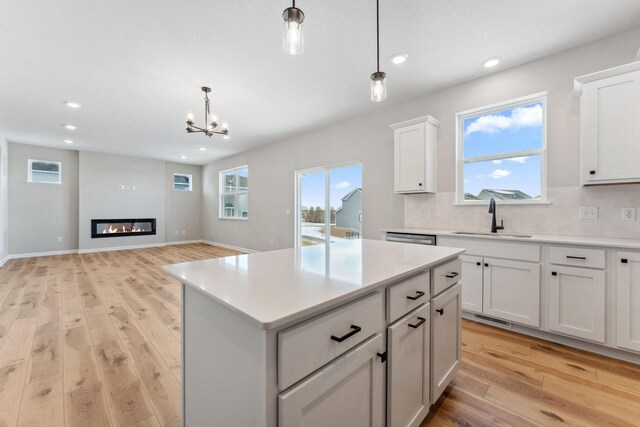 kitchen featuring light wood-style floors, tasteful backsplash, a chandelier, a sink, and light countertops