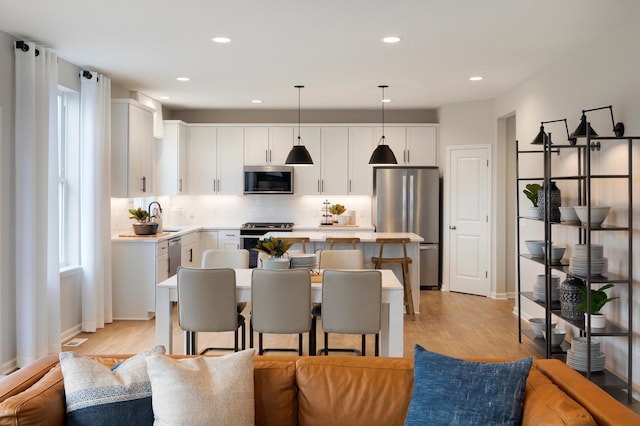 kitchen with open floor plan, a center island, stainless steel appliances, white cabinets, and light countertops