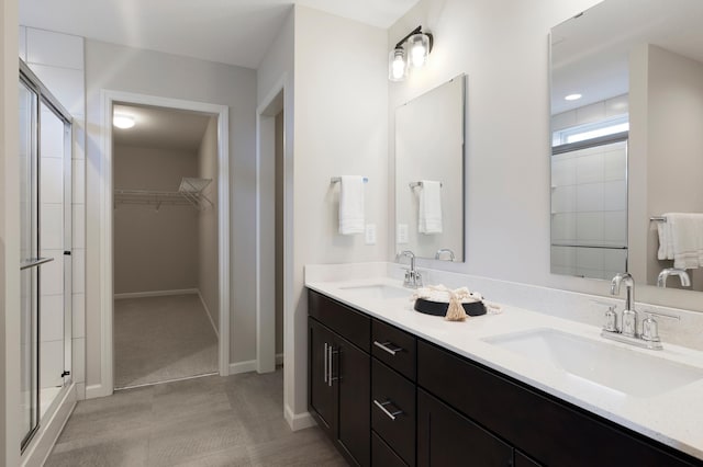 bathroom with a spacious closet, a stall shower, and a sink