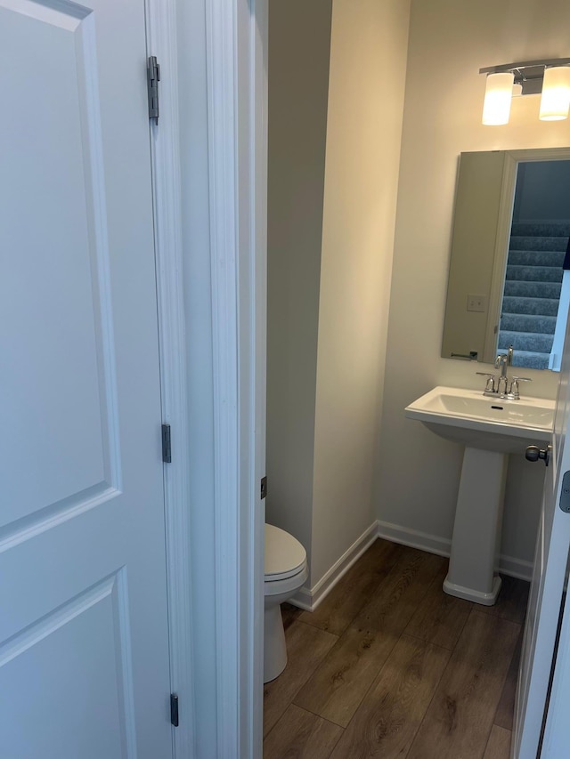 half bath featuring a sink, toilet, baseboards, and wood finished floors