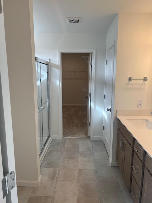 full bath featuring visible vents, a walk in closet, a shower stall, baseboards, and vanity