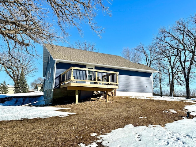 snow covered property featuring roof with shingles and a wooden deck