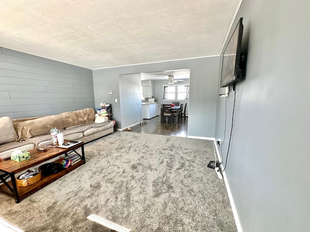 carpeted living room with ceiling fan, wooden walls, baseboards, and a textured ceiling