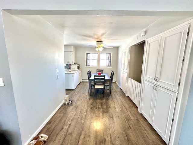 dining area featuring a baseboard heating unit, dark wood-type flooring, a ceiling fan, and baseboards