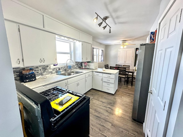 kitchen with black range with gas cooktop, a peninsula, a sink, backsplash, and freestanding refrigerator