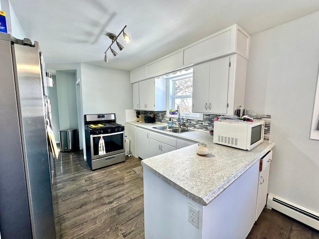 kitchen featuring a baseboard heating unit, a peninsula, a sink, appliances with stainless steel finishes, and tasteful backsplash