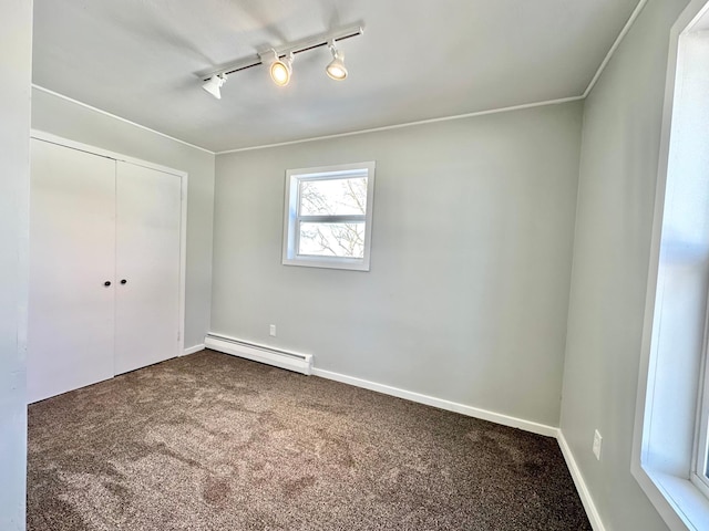 unfurnished bedroom featuring a closet, baseboards, a baseboard radiator, dark colored carpet, and track lighting