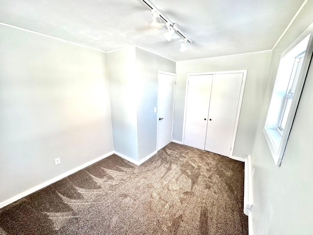 unfurnished bedroom with carpet, track lighting, baseboards, and a closet