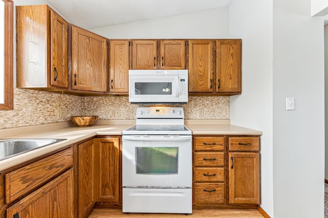 kitchen featuring tasteful backsplash, light countertops, lofted ceiling, brown cabinetry, and white appliances