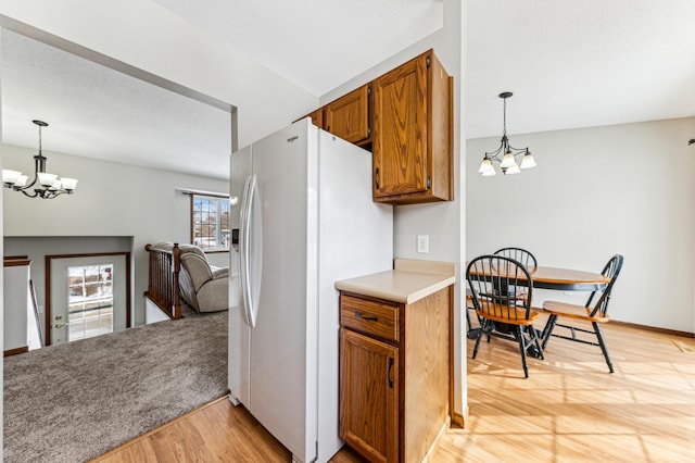 kitchen with light countertops, brown cabinets, white refrigerator with ice dispenser, light wood-style floors, and a notable chandelier