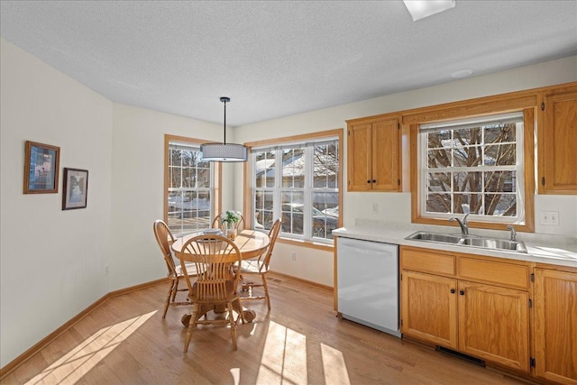 kitchen with light countertops, light wood-style floors, white dishwasher, a textured ceiling, and a sink