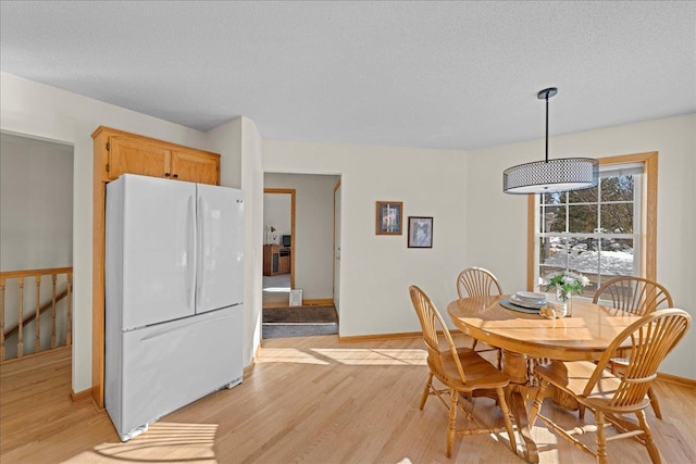 dining room with baseboards, light wood-type flooring, and a textured ceiling