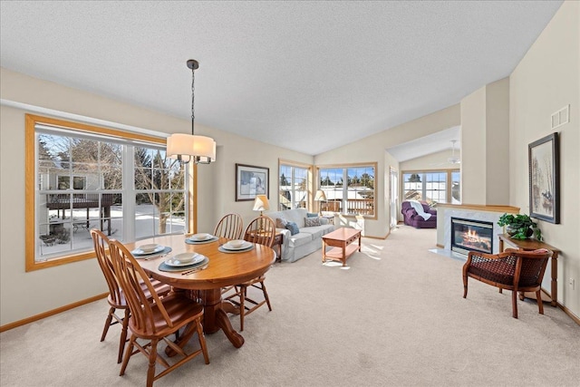 carpeted dining space featuring vaulted ceiling, a fireplace with flush hearth, baseboards, and visible vents