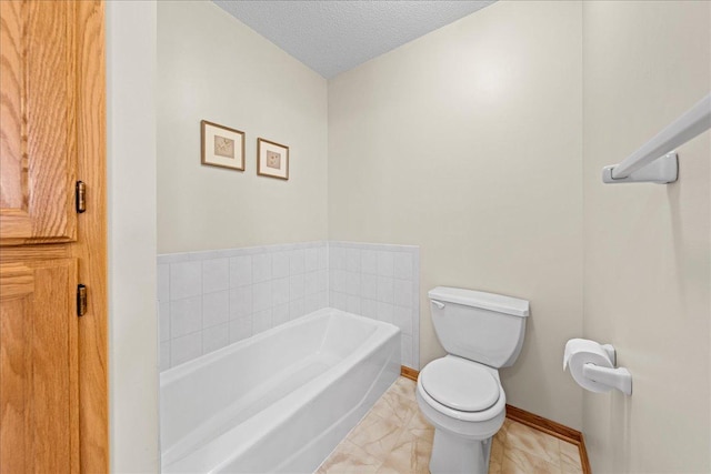 bathroom featuring toilet, a bath, baseboards, and a textured ceiling