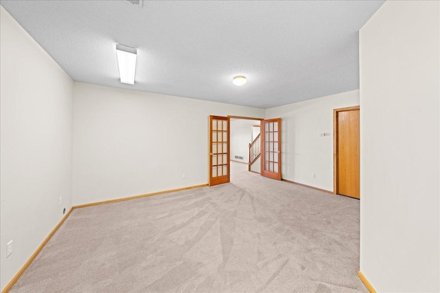 carpeted spare room with french doors, baseboards, and a textured ceiling