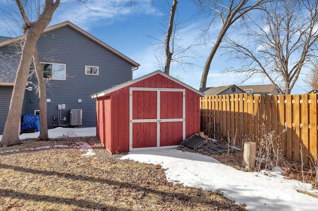 snow covered structure featuring a storage shed, an outdoor structure, and fence