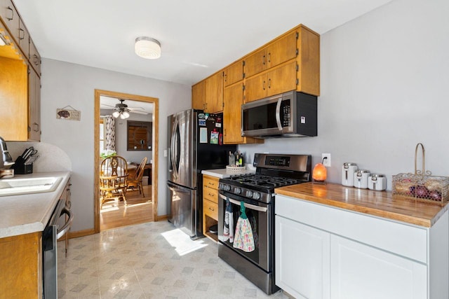 kitchen with a sink, stainless steel appliances, light countertops, baseboards, and ceiling fan