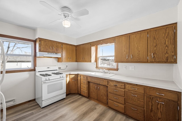 kitchen with light wood finished floors, gas range gas stove, under cabinet range hood, light countertops, and a sink