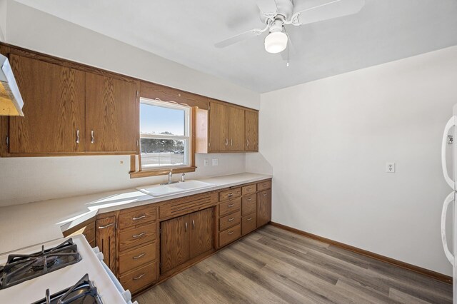 kitchen featuring light wood-type flooring, a sink, white appliances, brown cabinetry, and light countertops