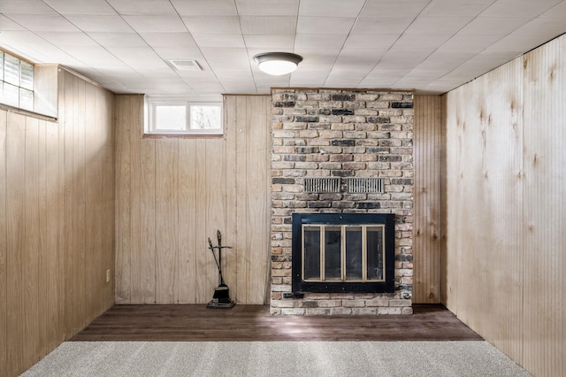 unfurnished living room with visible vents, a fireplace, wooden walls, and wood finished floors