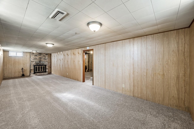 basement featuring a brick fireplace, visible vents, carpet floors, and wood walls