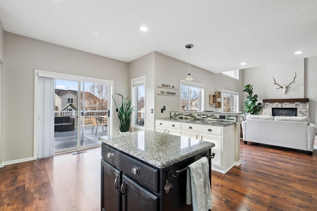 kitchen with light stone counters, a fireplace, dark wood-style flooring, hanging light fixtures, and a center island