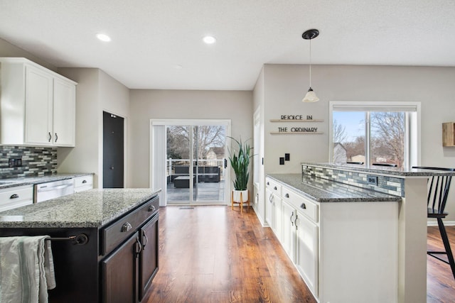 kitchen with a wealth of natural light, wood finished floors, dishwasher, and a breakfast bar area