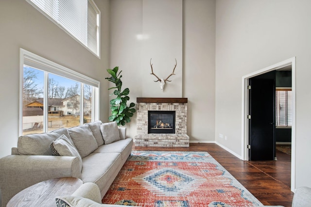 living area featuring baseboards, a high ceiling, a brick fireplace, and dark wood finished floors