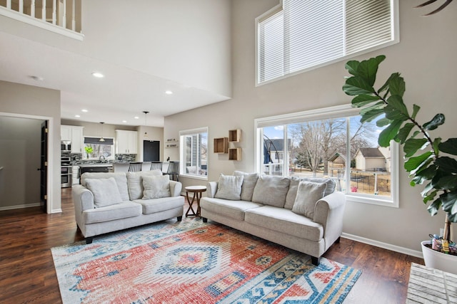 living area featuring dark wood-style floors, recessed lighting, baseboards, and a towering ceiling