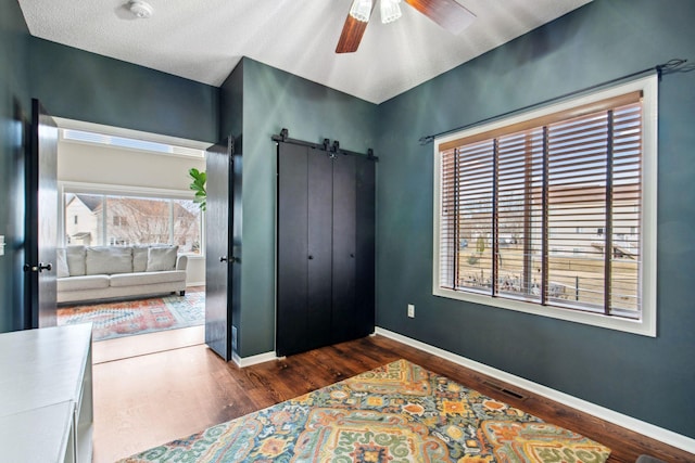 bedroom featuring a barn door, wood finished floors, baseboards, and ceiling fan