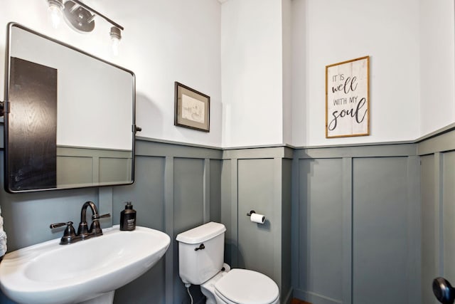 half bath featuring a sink, a wainscoted wall, toilet, and a decorative wall