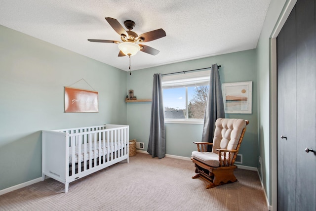 bedroom featuring a textured ceiling, a closet, carpet floors, a nursery area, and baseboards