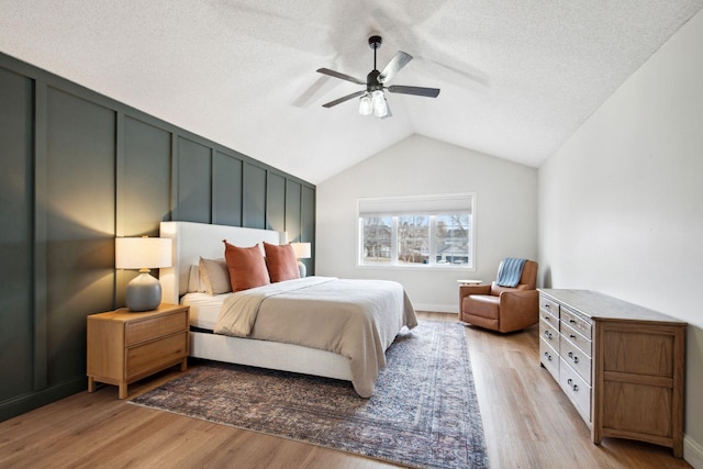 bedroom featuring a ceiling fan, a textured ceiling, vaulted ceiling, and light wood finished floors