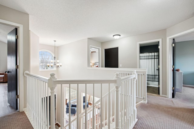 hallway with baseboards, carpet, a chandelier, an upstairs landing, and a textured ceiling