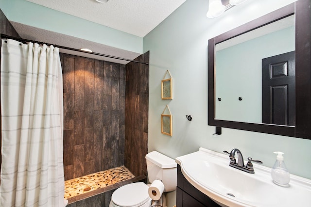 bathroom featuring vanity, toilet, a tile shower, and a textured ceiling