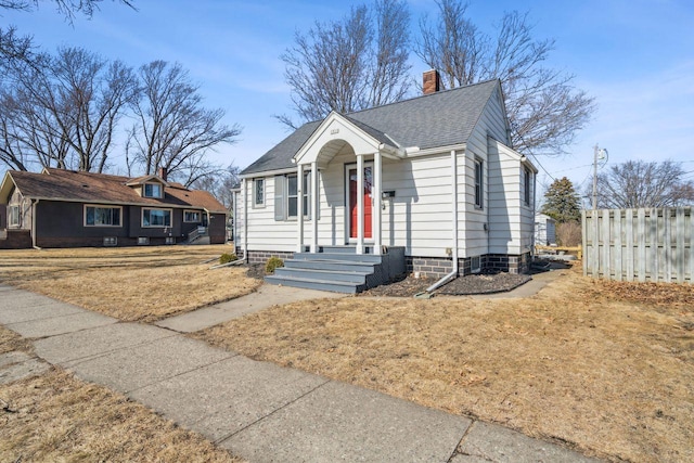 bungalow with a shingled roof, a chimney, a front yard, and fence